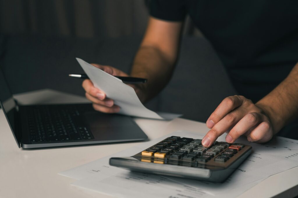 Asian man using calculator to calculate expenses while holding family bills at his home.